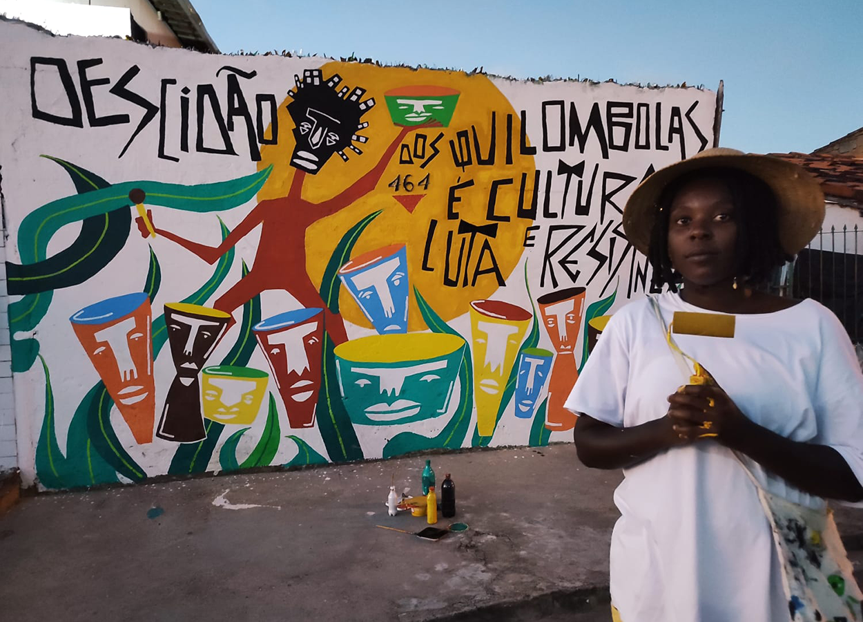 Larissa Vieira. Ao fundo, mural feito por ela em homenagem ao bloco afro Descidão dos Quilombolas. Foto: divulgação